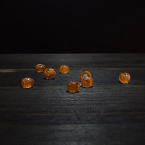 Rund orange glaspärla - Round orange glaspärlor (5mm) arrangerad on dark trä. Translucent amber glass med warm golden tone, perfect for jewelry crafting.