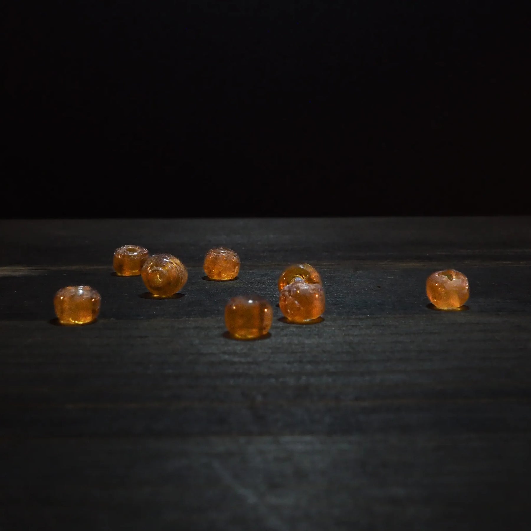 Rund orange glaspärla - Round orange glaspärlor (5mm) visad on dark trä surface. Translucent amber glaspärlor for jewelry and craft projects.