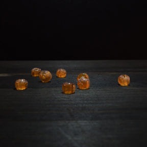 Rund orange glaspärla - Round orange glaspärlor (5mm) visad on dark trä surface. Translucent amber glaspärlor for jewelry and craft projects.