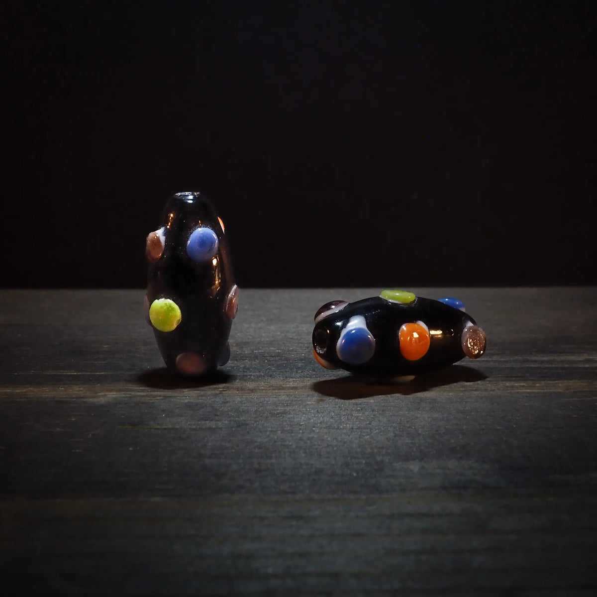 Fyra mörka glaspärlor med färgade prickar omgivna av gröna växtblad på naturlig mörk bakgrund