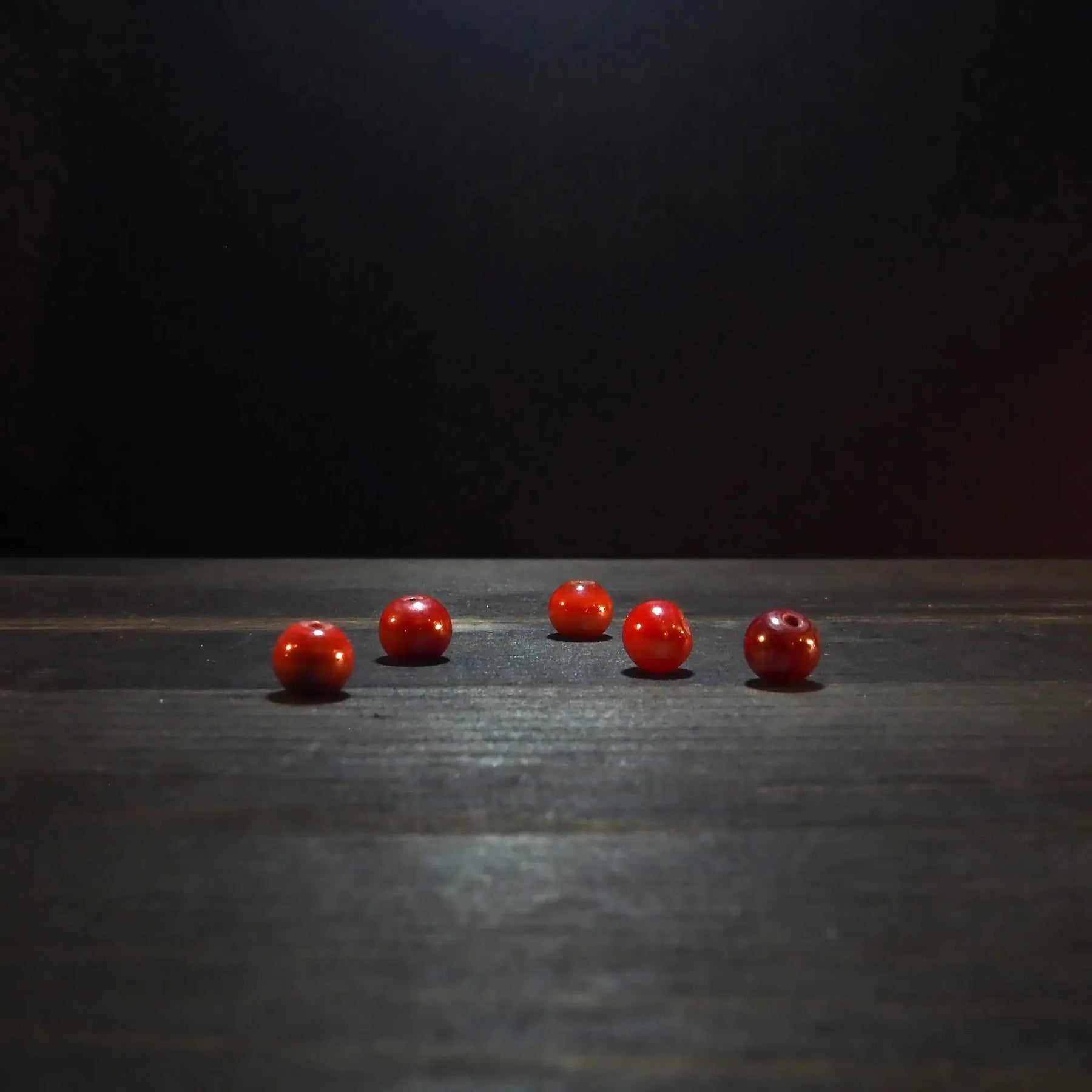 Fem röda glaspärlor på träyta