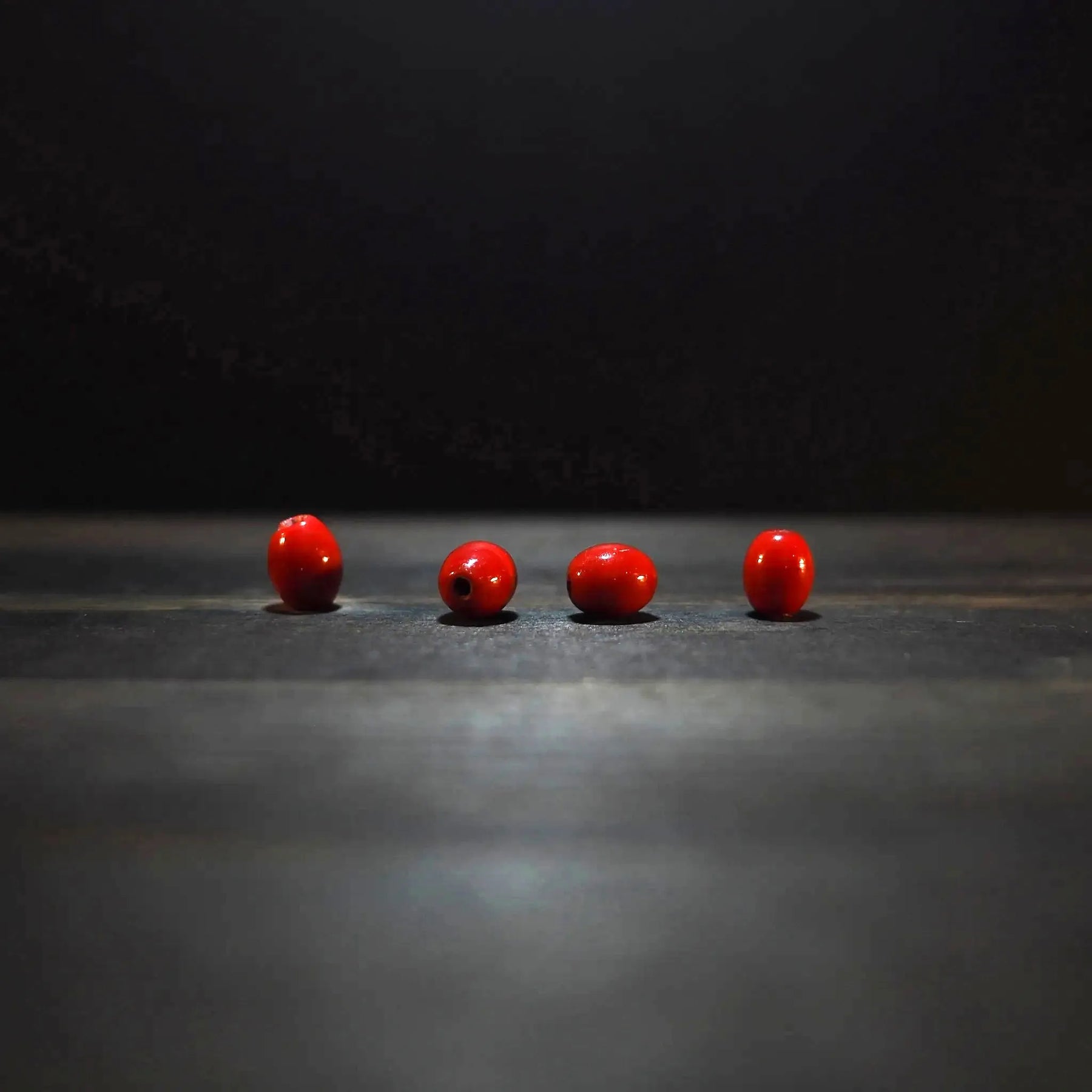 Fyra röda ovalglaspärlor, 7x10mm, på träyta