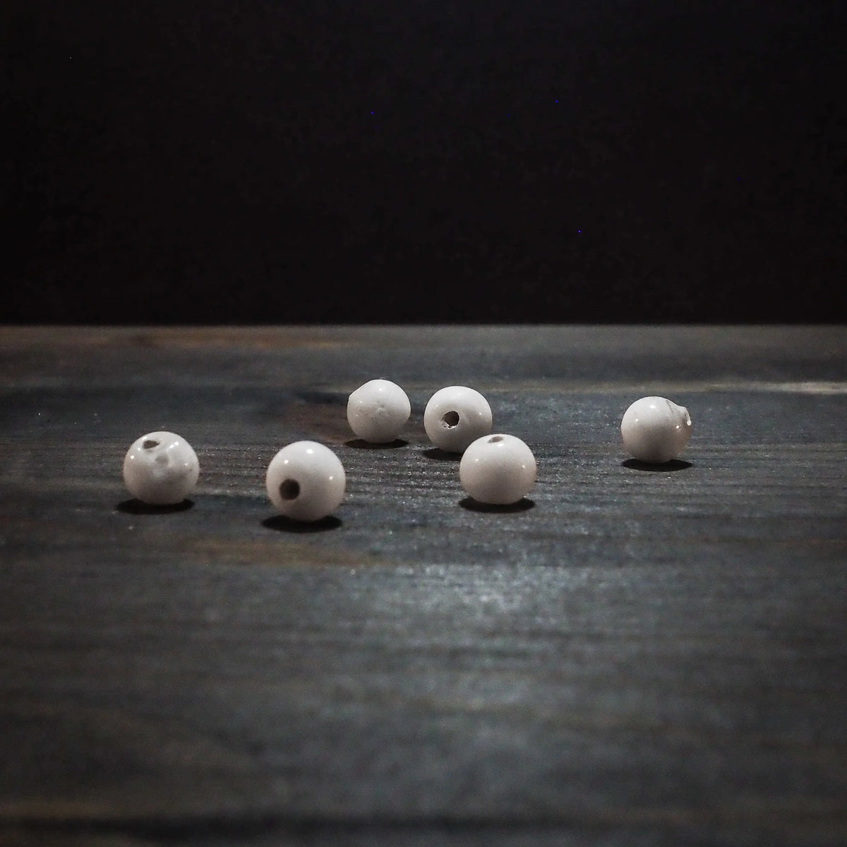 Sex vita glaspärlor, runda och cirka 6mm med genomgående hål, fotograferade på vit bakgrund för tydlig produktöversikt