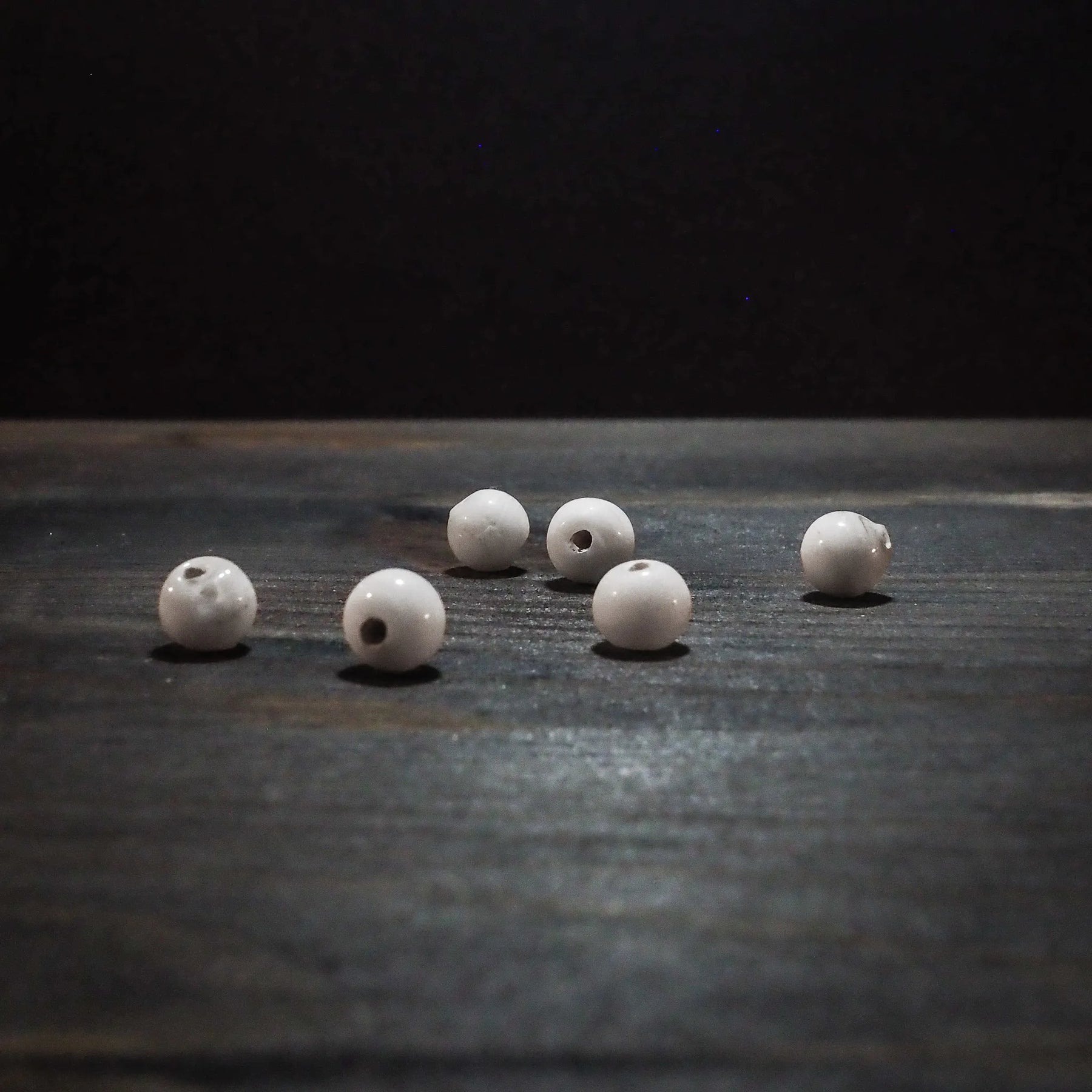 Sex vita glaspärlor, runda och cirka 6mm med genomgående hål, fotograferade på vit bakgrund för tydlig produktöversikt