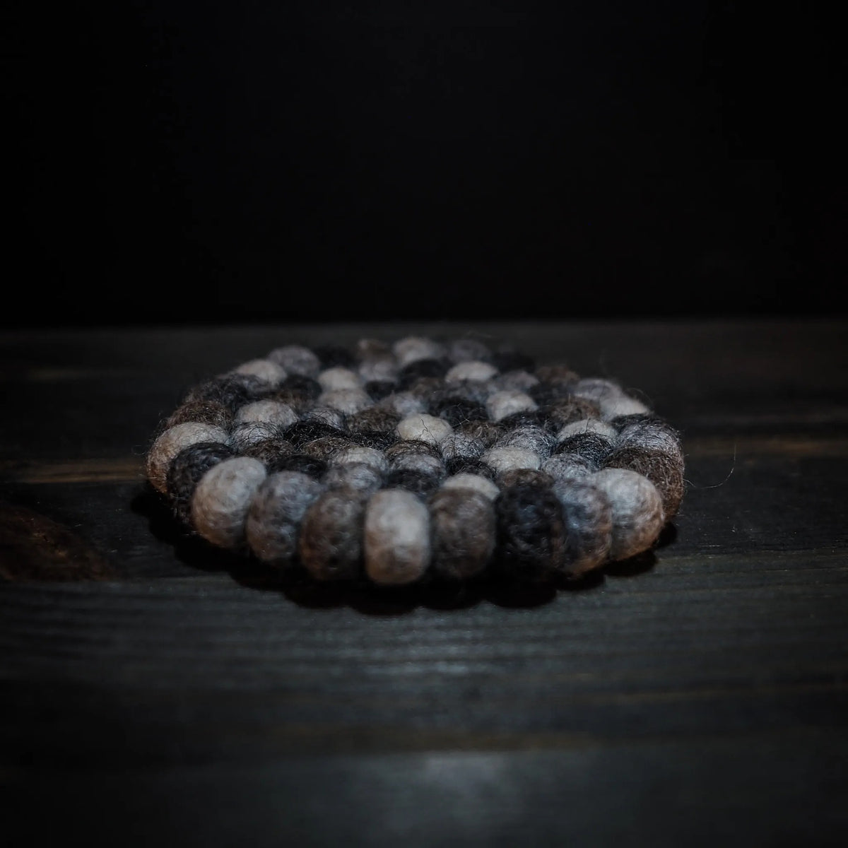 Round felt coaster with black and white wool balls in circular pattern, photographed at ground level
