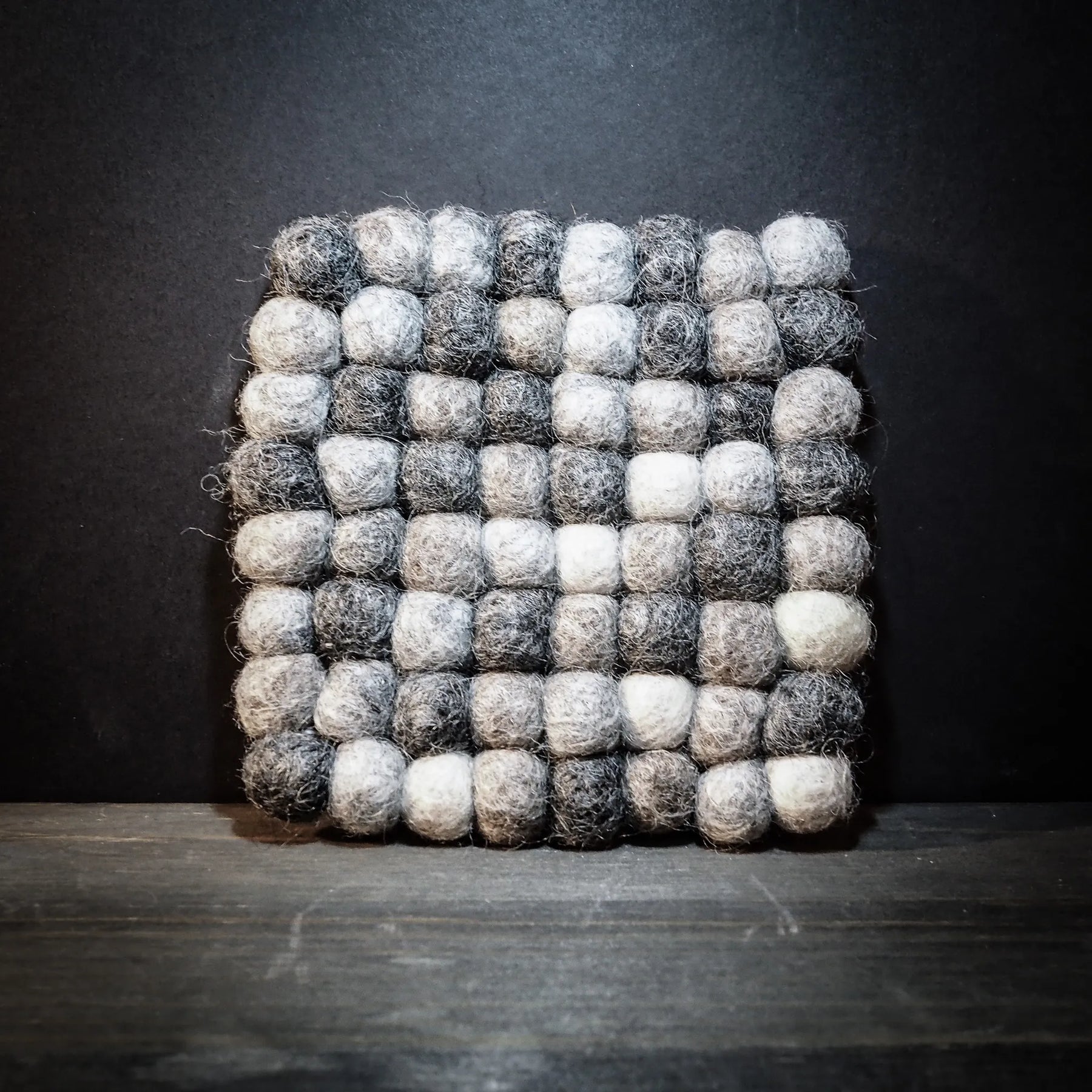 Handgjort filtrat underlägg med svart och vita ullkulor i rutnätsmönster