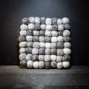 Handgjort filtrat underlägg med svart och vita ullkulor i rutnätsmönster