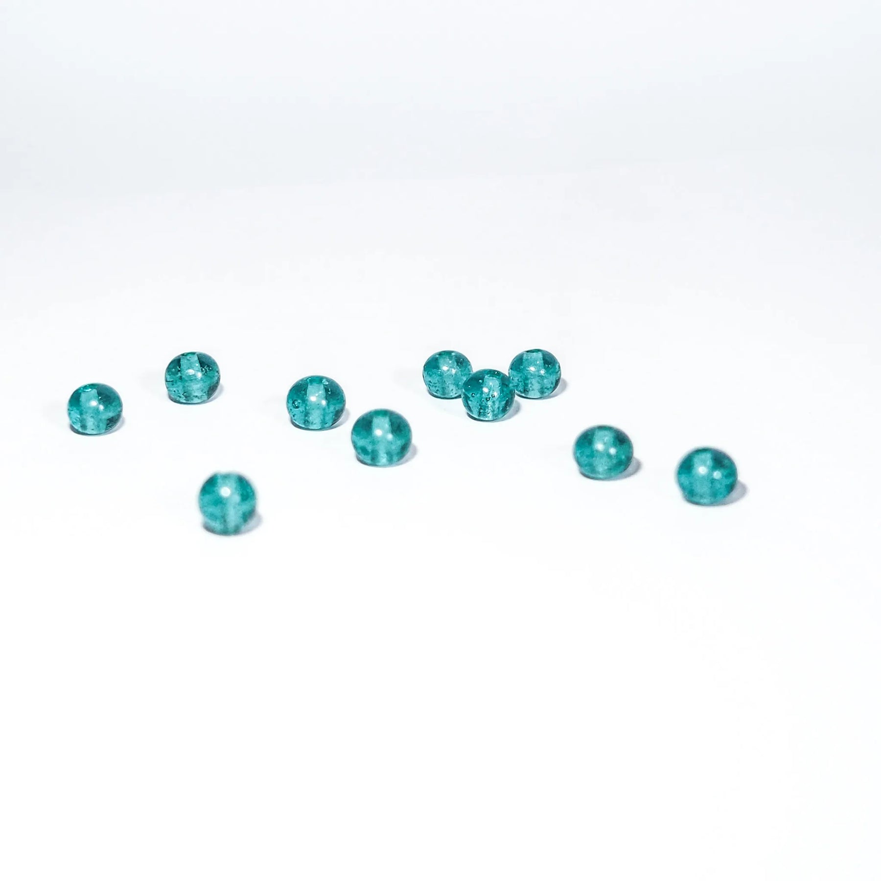 Ungefär 11 små turkosglaspärlor på vit yta