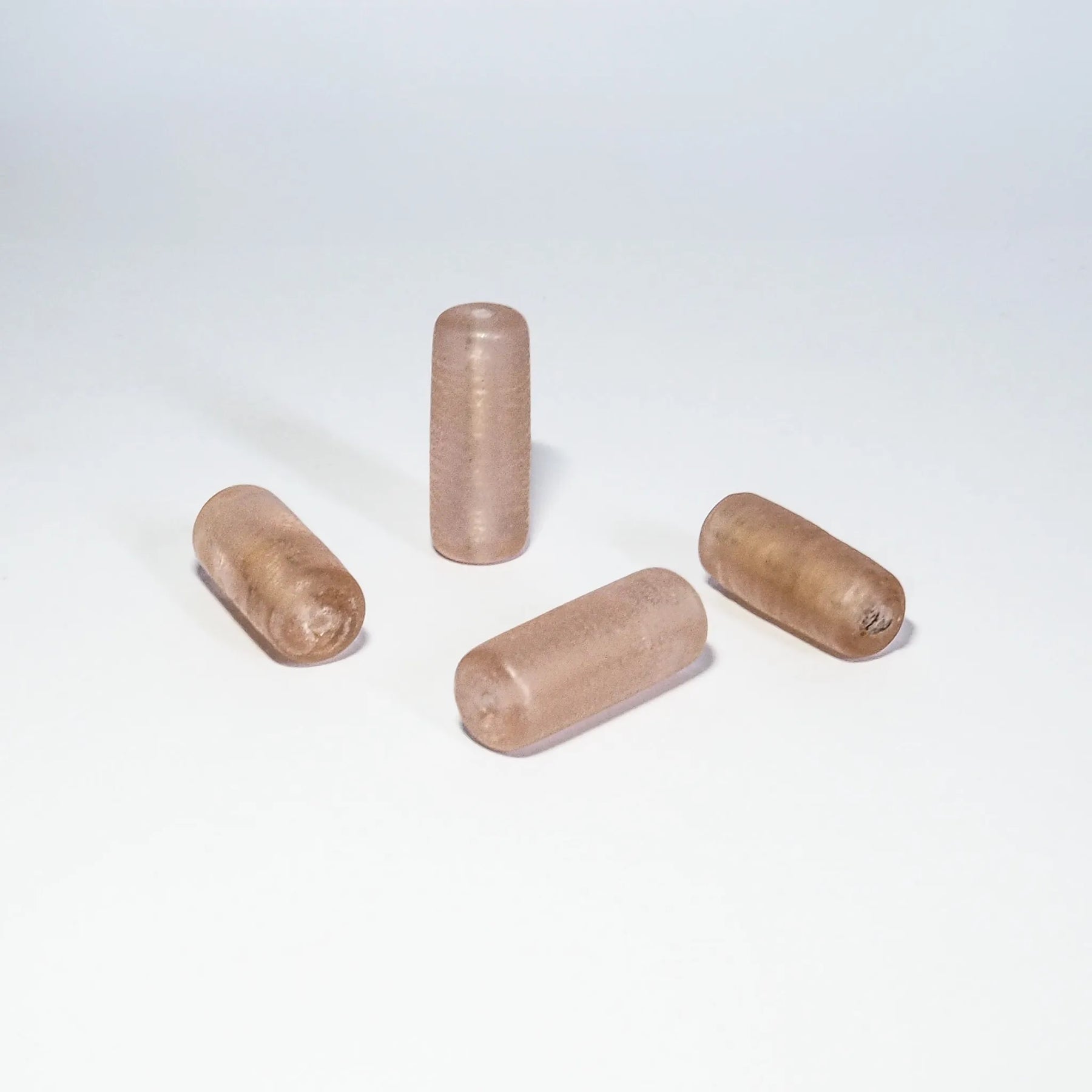 Fyra ljusrosa glaspärlor på neutral bakgrund. Cylinderformade pärlor i varierande nyanser av rosa och beige.