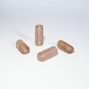 Fyra ljusrosa glaspärlor på neutral bakgrund. Cylinderformade pärlor i varierande nyanser av rosa och beige.