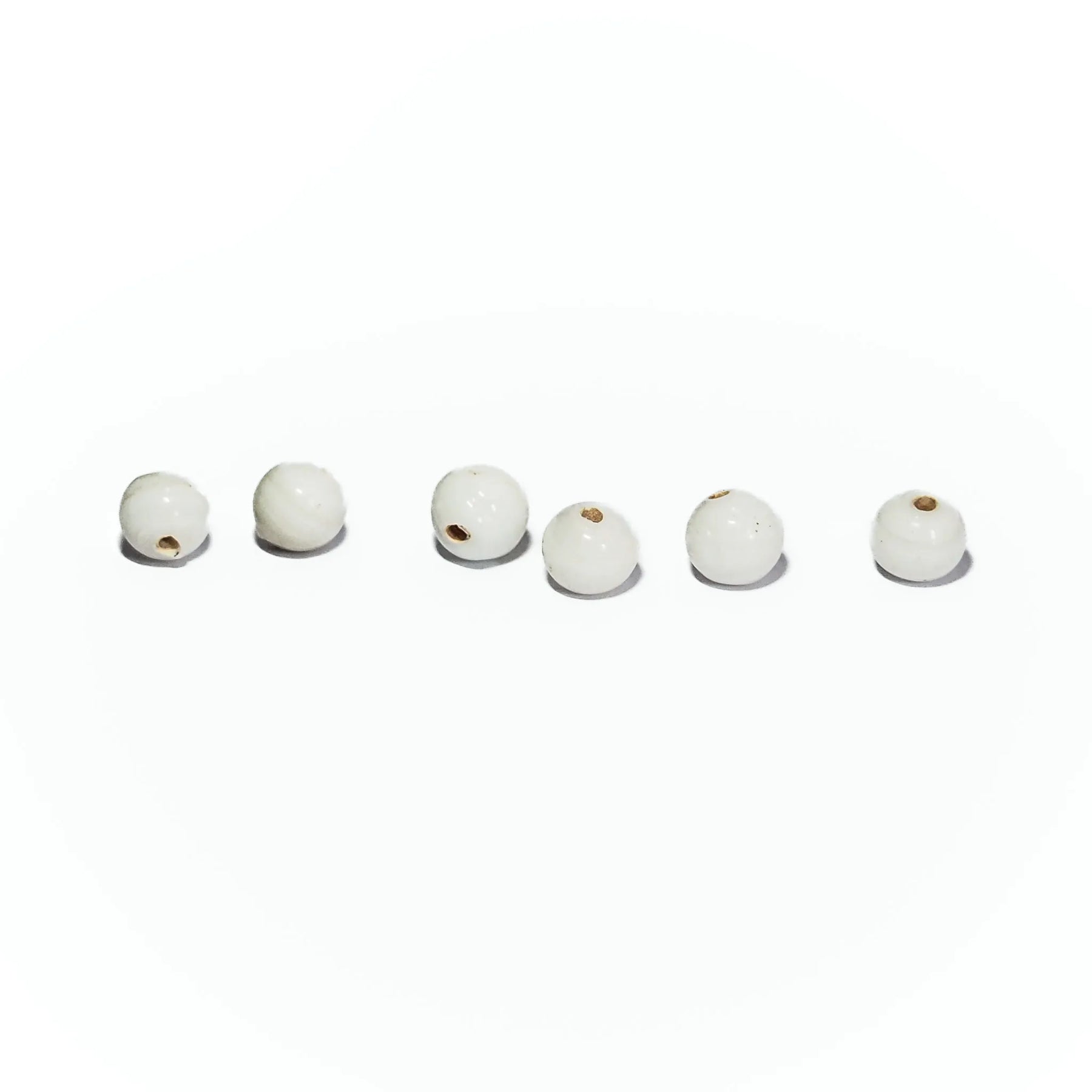 Sex vita glaspärlor på ljus bakgrund, runda cirka 6mm med genomgående hål, visar naturlig glasstruktur och skuggor