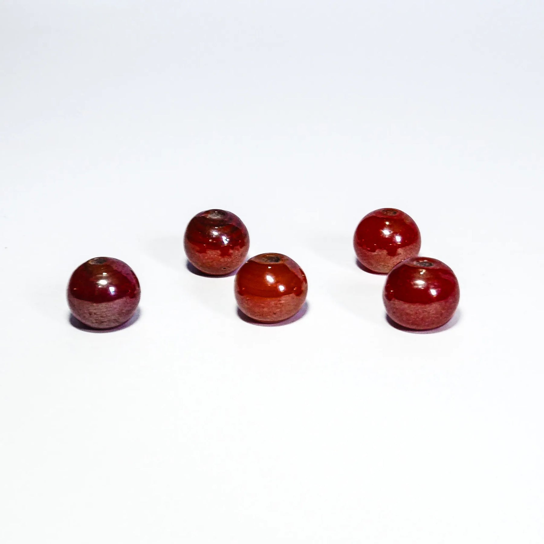 Fem röda och gräddfärgade strukturerade glaspärlor på vit bakgrund