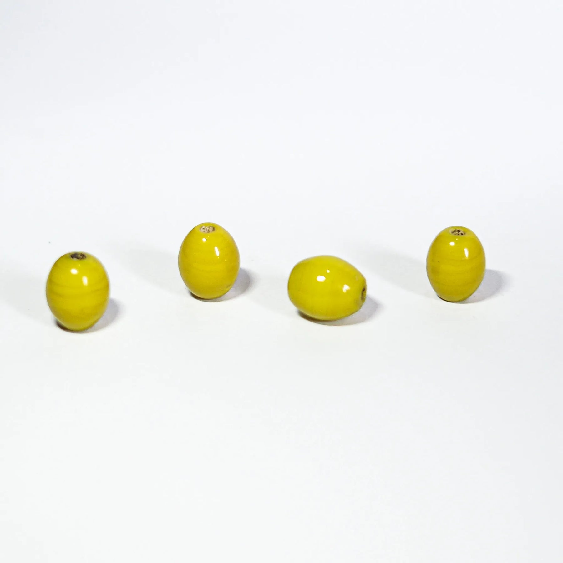 Fyra gula ovalglaspärlor, 7x10mm, på ljus bakgrund