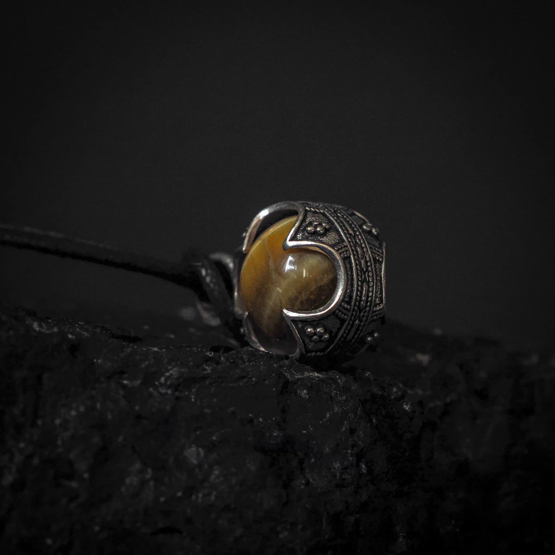 Två mässinghängen gotlandskula med tigeröga på svarta läderband. Båda hängena har identiska guldtonande mässingsmonterings med tigeroögstenar som skiner i varma guldbruna nyanser mot mörk stenig bakgrund.