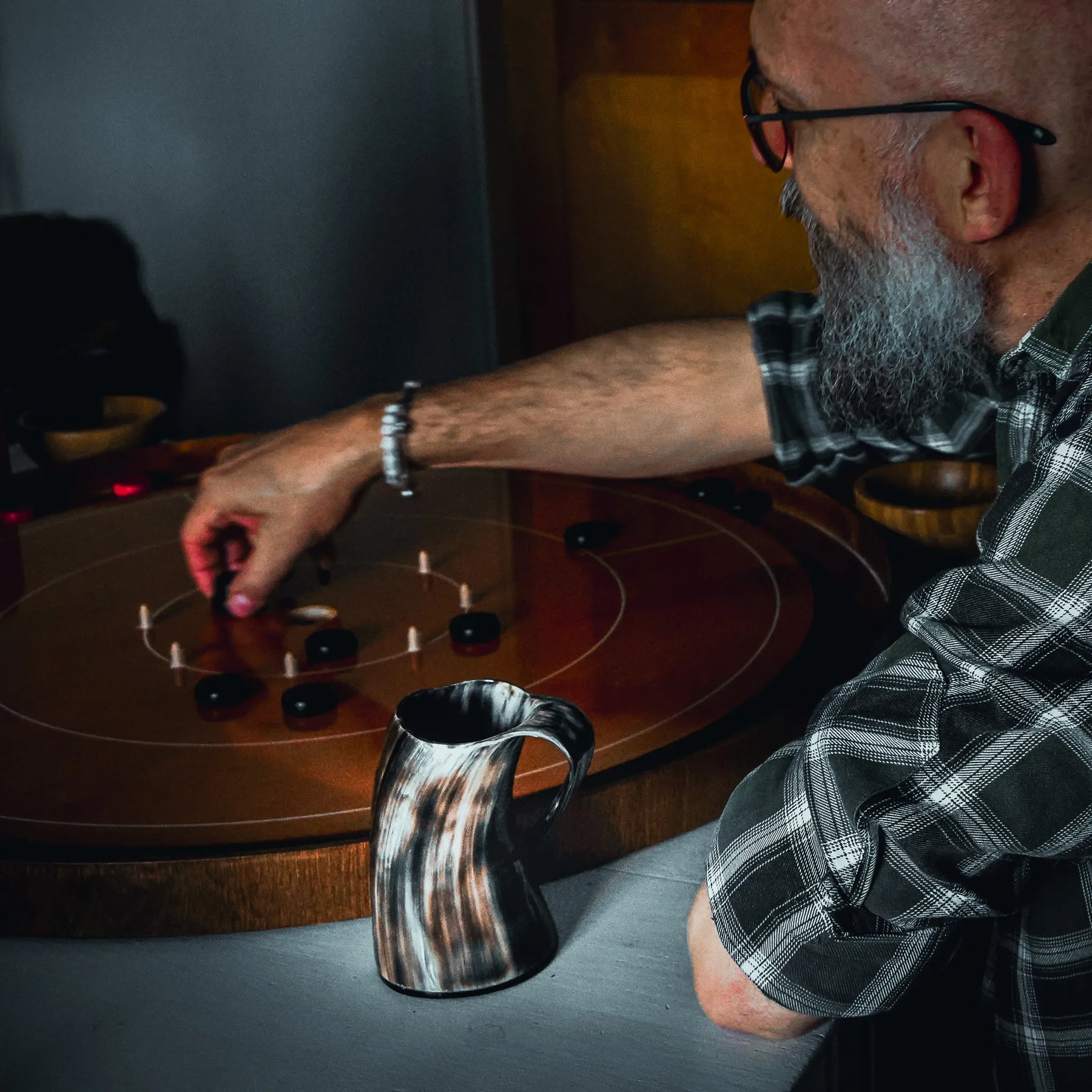 Man med skägg hålls polerad hornmugg vid träbord i hemlig miljö med skivspelare i bakgrunden