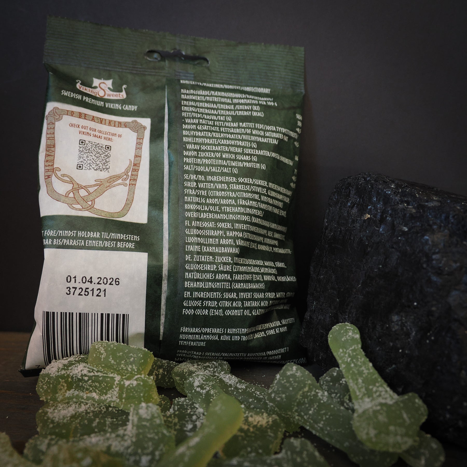 Viking Sweets Iduns syrliga äpplen, förpackning med godisbitar och dekorativa Mjölnirsköldar på mörk bakgrund.