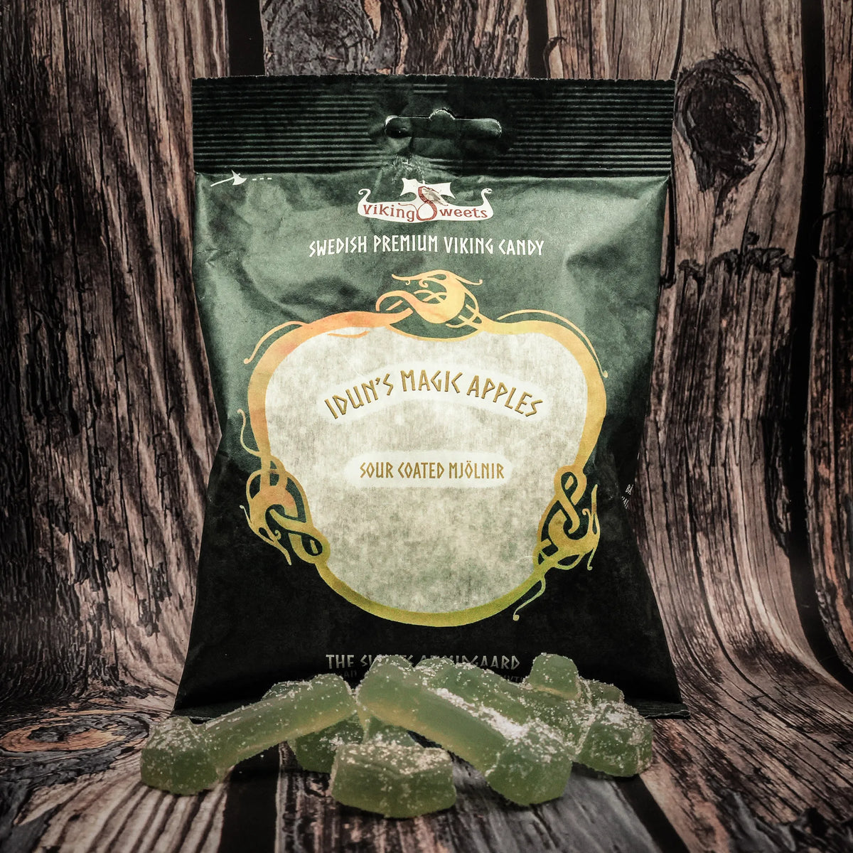 Viking Sweets Iduns syrliga äpplen, förpackning med godisbitar och dekorativa Mjölnirsköldar på mörk bakgrund.
