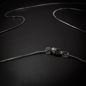 Silverfärgad kirurgisk stålkedja 55cm, 1mm tjock, nickelfri, med slang-mönstrad länkstruktur visad på texturerad yta