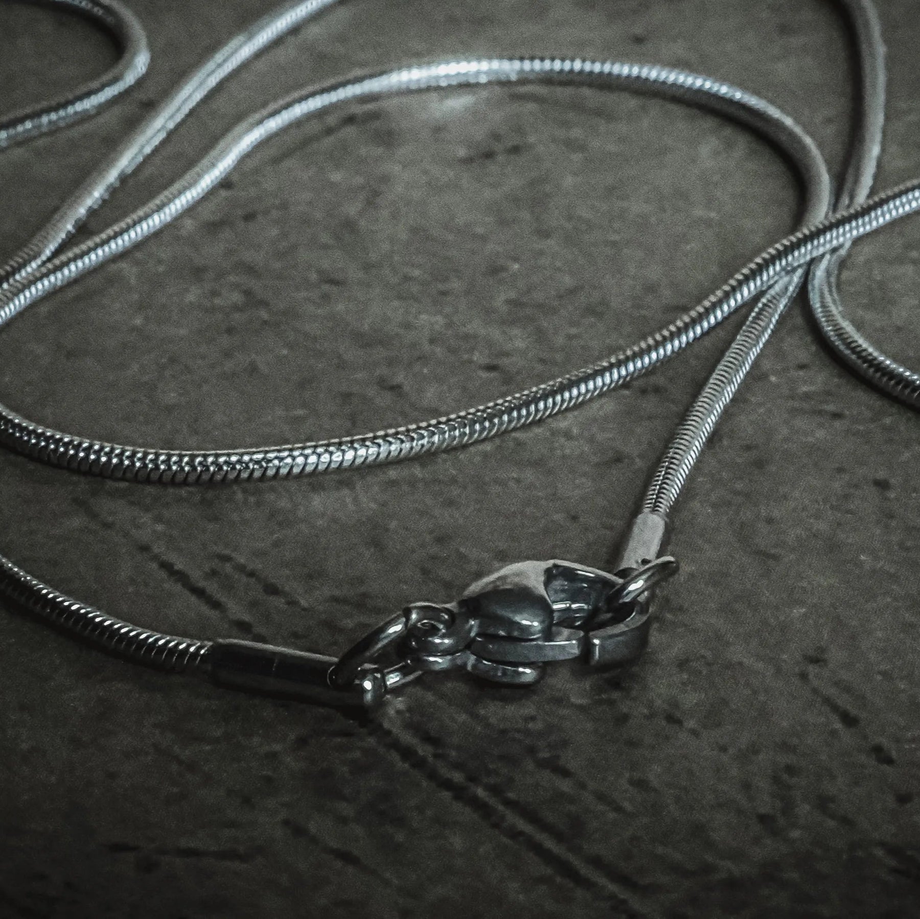 Silverfärgad kirurgisk stålkedja 55cm med synlig hummerlås, visad från ovan med slang-mönstrad länkstruktur