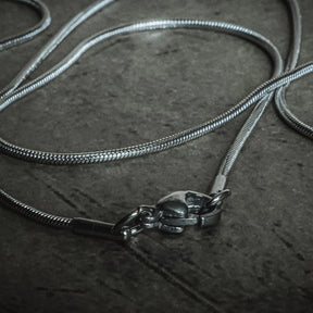Silverfärgad kirurgisk stålkedja 55cm med synlig hummerlås, visad från ovan med slang-mönstrad länkstruktur
