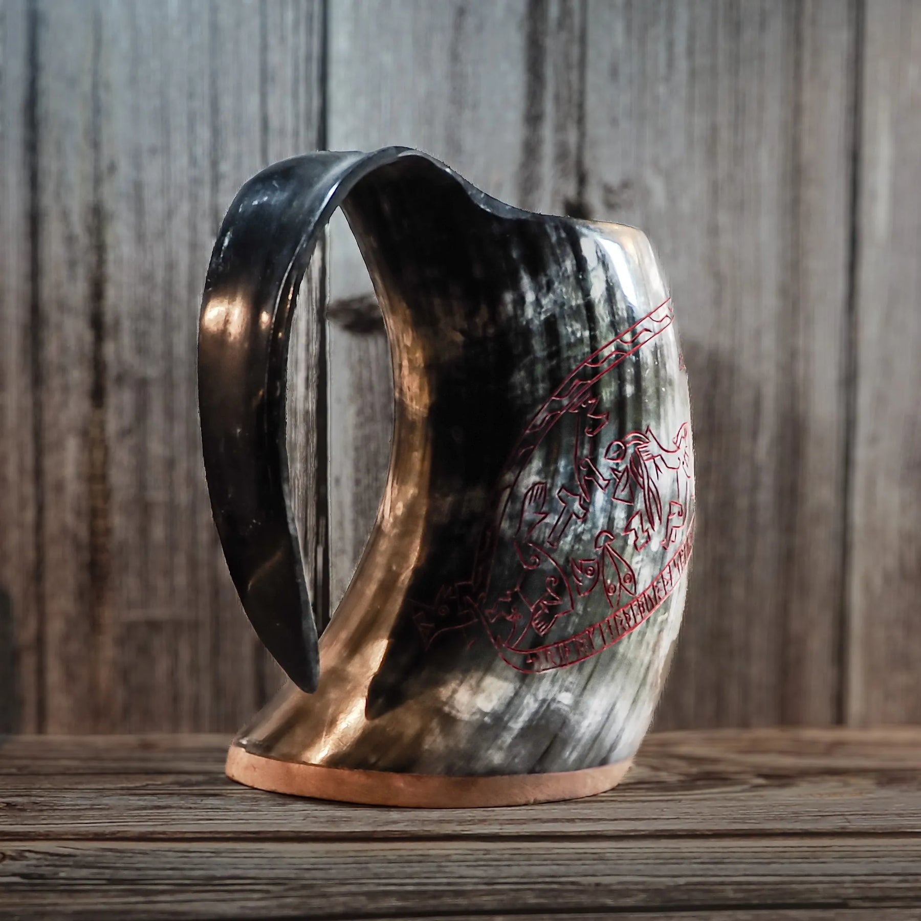 Trevärtsvy av graverad ölmugg av horn med Sigurdsagan-motiv. Muggen är svart polerad horn med guldig gravering som visar flera narrative scener från Norse-mytologin. Handtaget och naturlig hornbård vid basen är väl synliga.