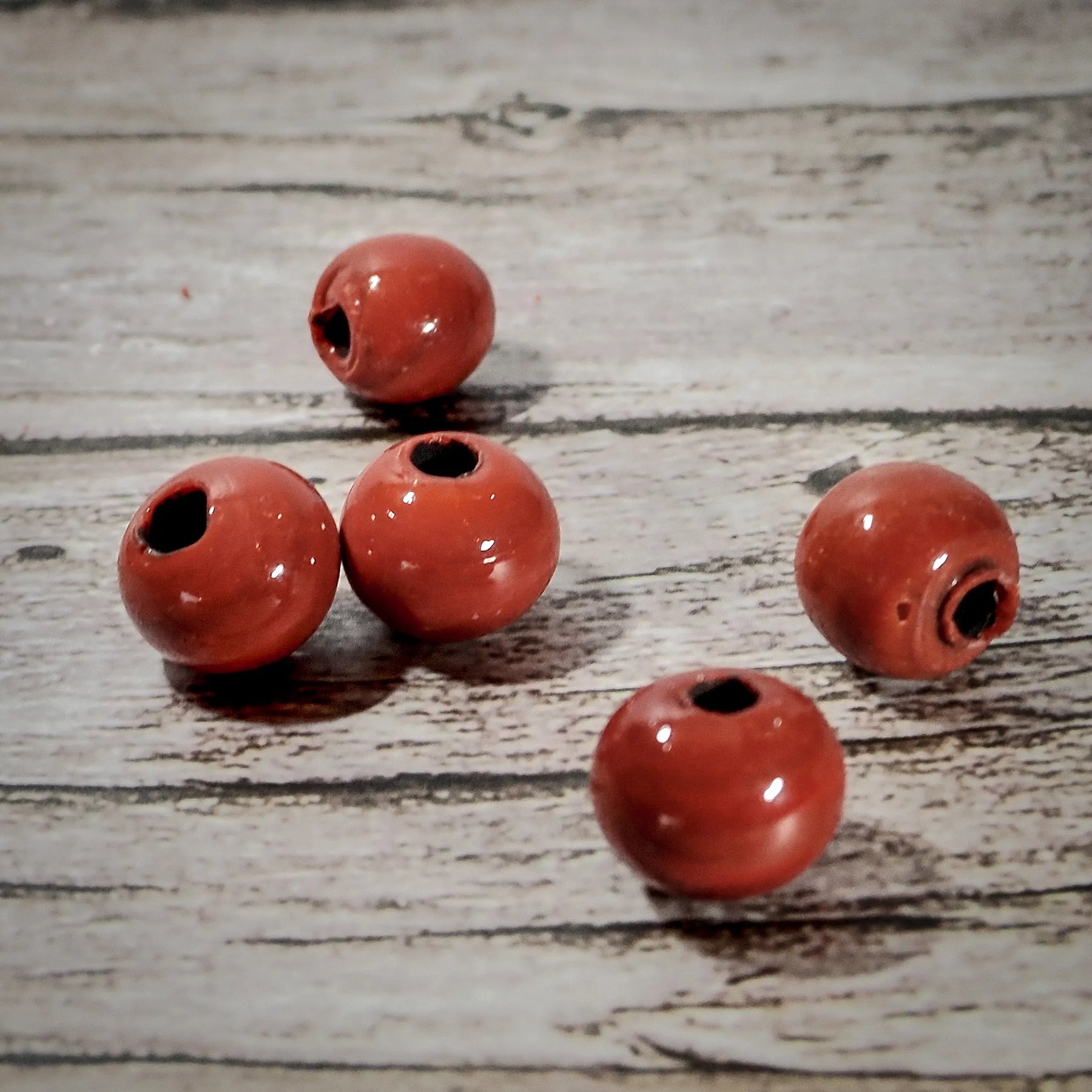 Röda glaspärlor, 6 mm, glansiga på trägolvsbakgrund, arrangement från olika vinklar