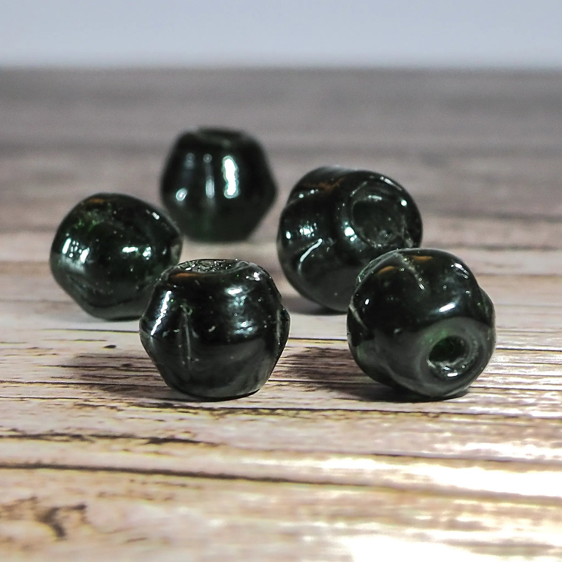 Mörkgrön melonpärla i mindre storlek, 6mm med 2mm hål. Translucent djupgrön glasyrta med blank finish. Fem exemplar visar pärlans rotationsgeometri på ljus bakgrund.