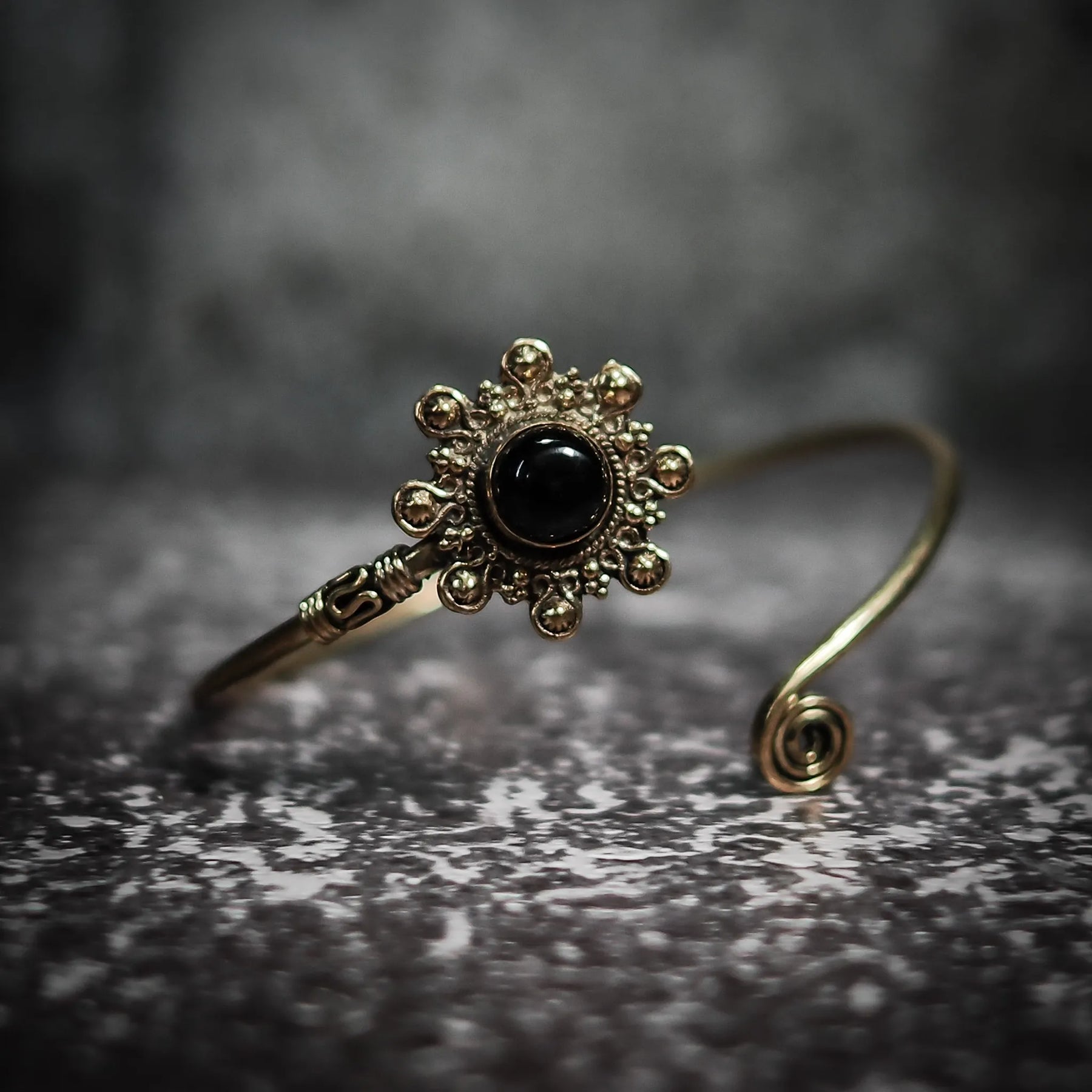 Mässingsarmband Sol med svart glansig halvädelssten, sol-motiv med tätt arrangerade ornamentala mässingskulor, dekorativ band