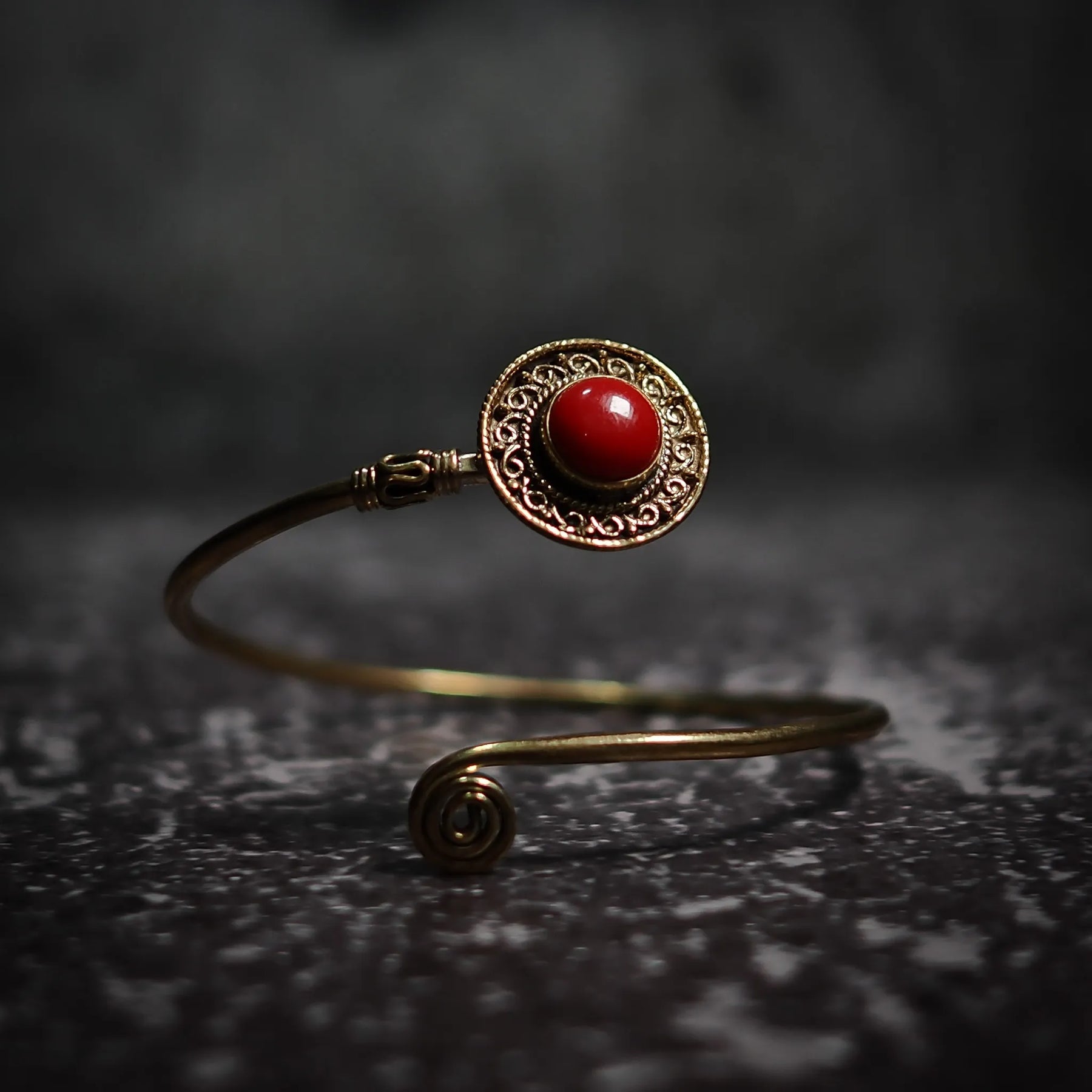Justerbar armband med djuprött cabochon-sten, dekorativ mässings­ornamentik och filigrerad antik-stil design.