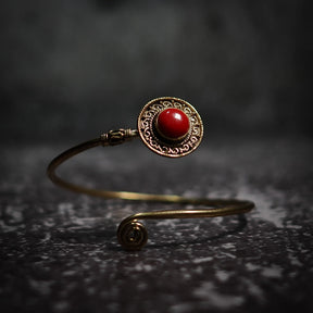 Justerbar armband med djuprött cabochon-sten, dekorativ mässings­ornamentik och filigrerad antik-stil design.