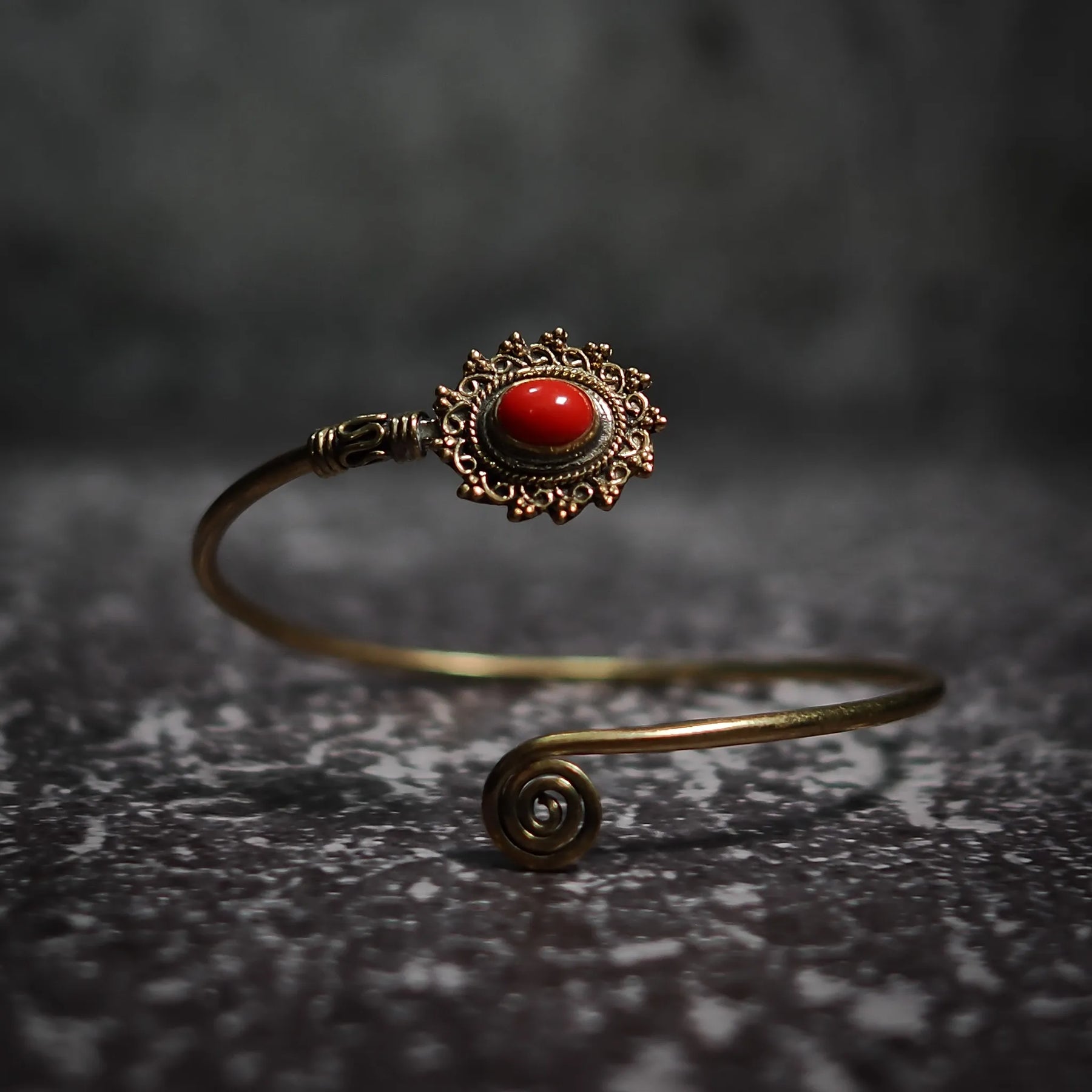 Vikingarmband i röd karneol med ornamenterad mässingfiligre och spiralformad terminal på mörk bakgrund