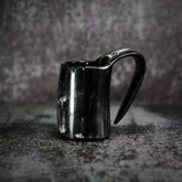 En handgjord espresso- och glöggmugg i horn med naturlig textur och polerad svart yta, fotograferad på grå betong.