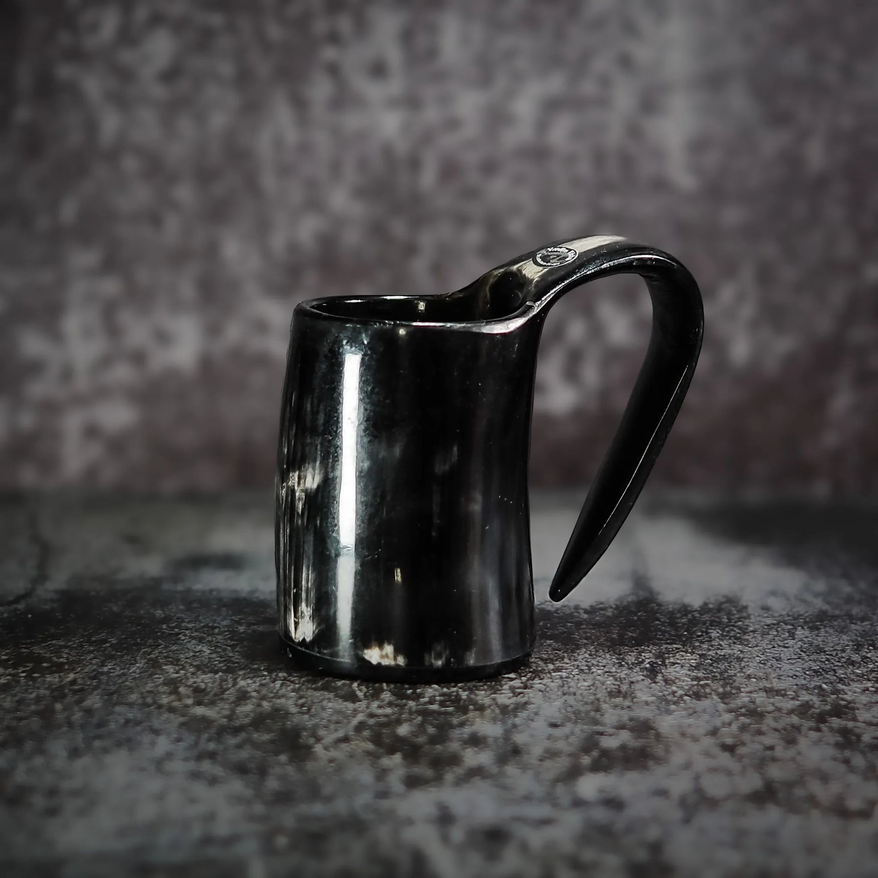 En handgjord espresso- och glöggmugg i horn med naturlig textur och polerad svart yta, fotograferad på grå betong.