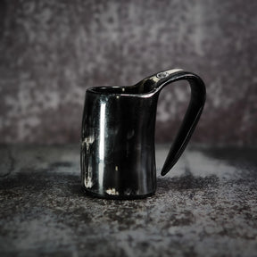 En handgjord espresso- och glöggmugg i horn med naturlig textur och polerad svart yta, fotograferad på grå betong.