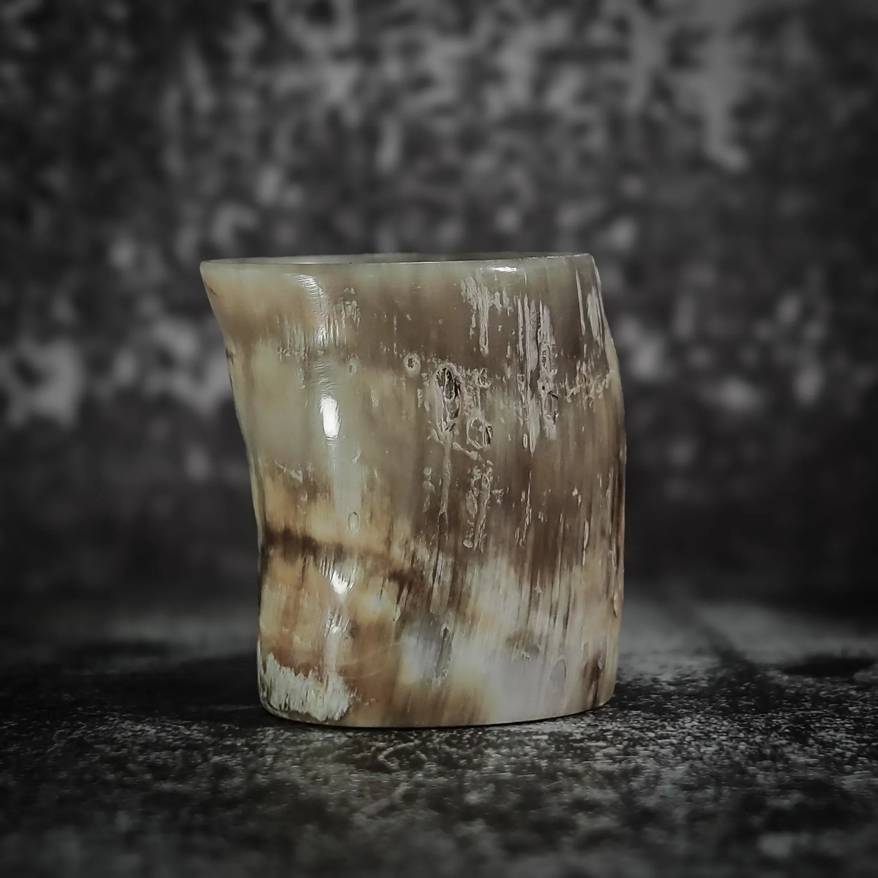 Whiskyglas i naturlig horn med synlig spräckled mönster och organisk textur, minimalistisk presentation