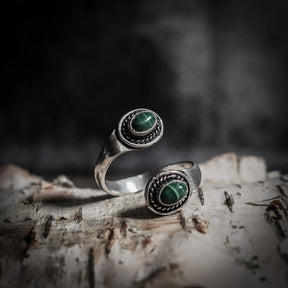 Spiralring med labradorit halvädel som reflekterar norrskenets aurora i blått och grönt, på weathered trä med mässing och dekorativ betoning.