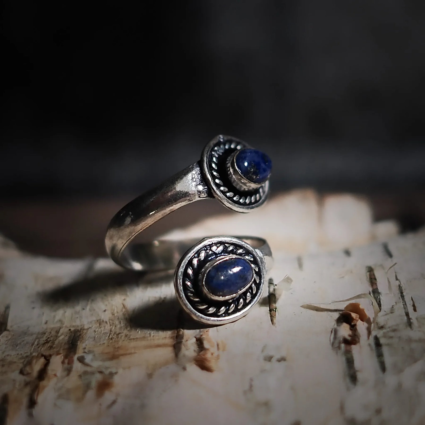Spiralring i justerbara mässing med labradorit som glimrar i norrskenets blågröna färger, elegant dekorativ kantbearbetning på trä.