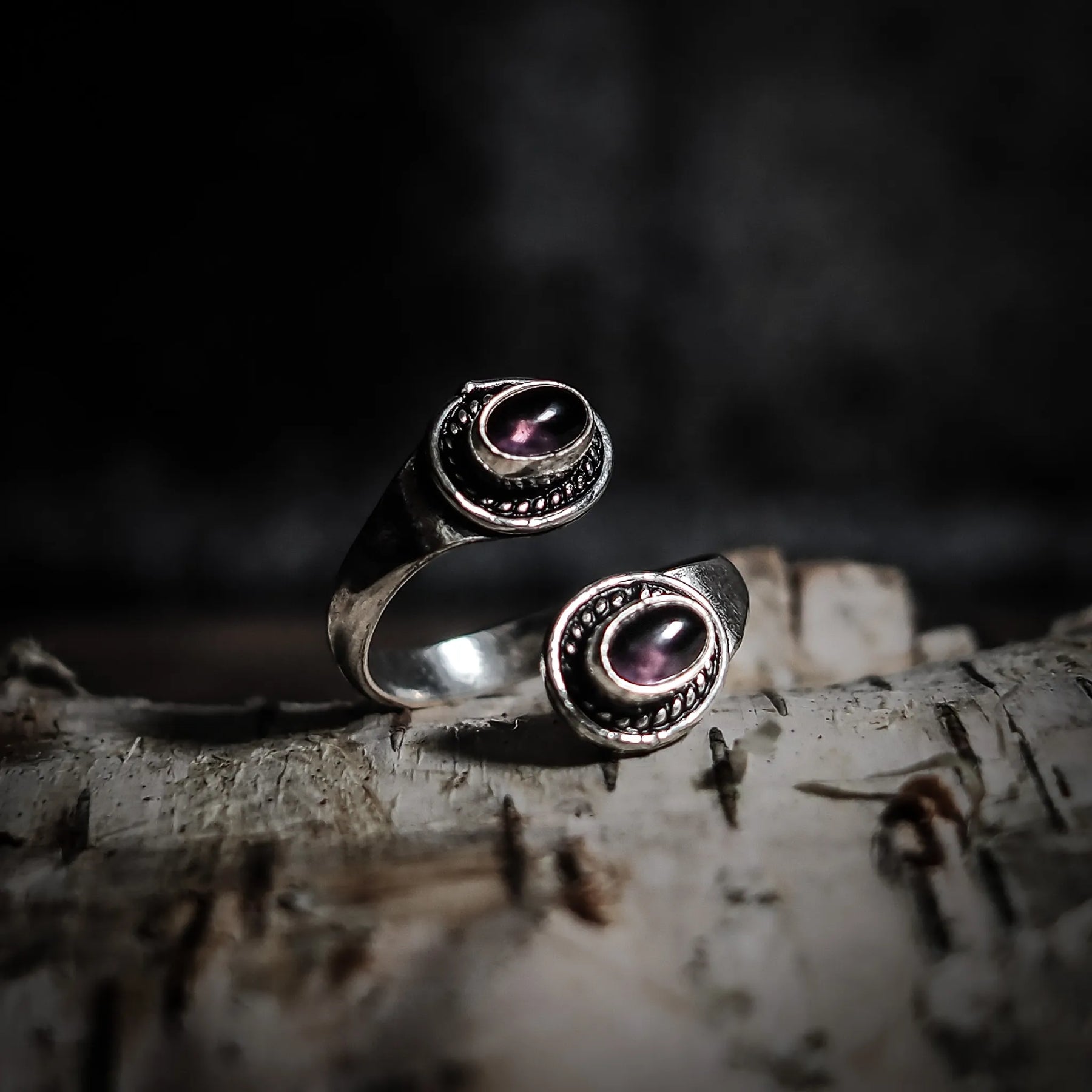 Spiralring i mässing med två labradoriter som visar rosa-lila glöd, lagd på trä