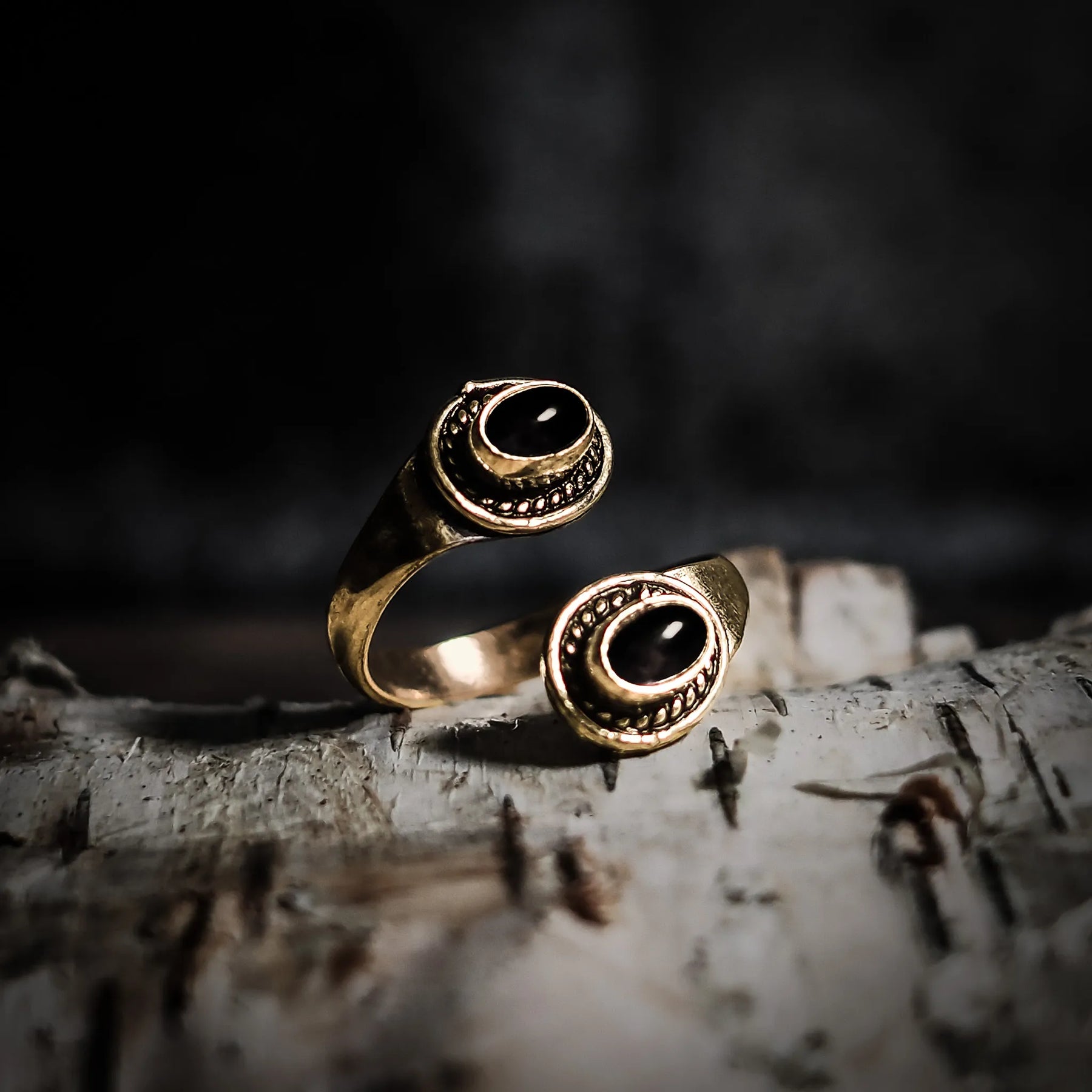 Spiralring i mässing med två labradoriter som skimrar grönblått, på trä med blommor