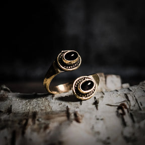 Spiralring i mässing med två labradoriter som skimrar grönblått, på trä med blommor
