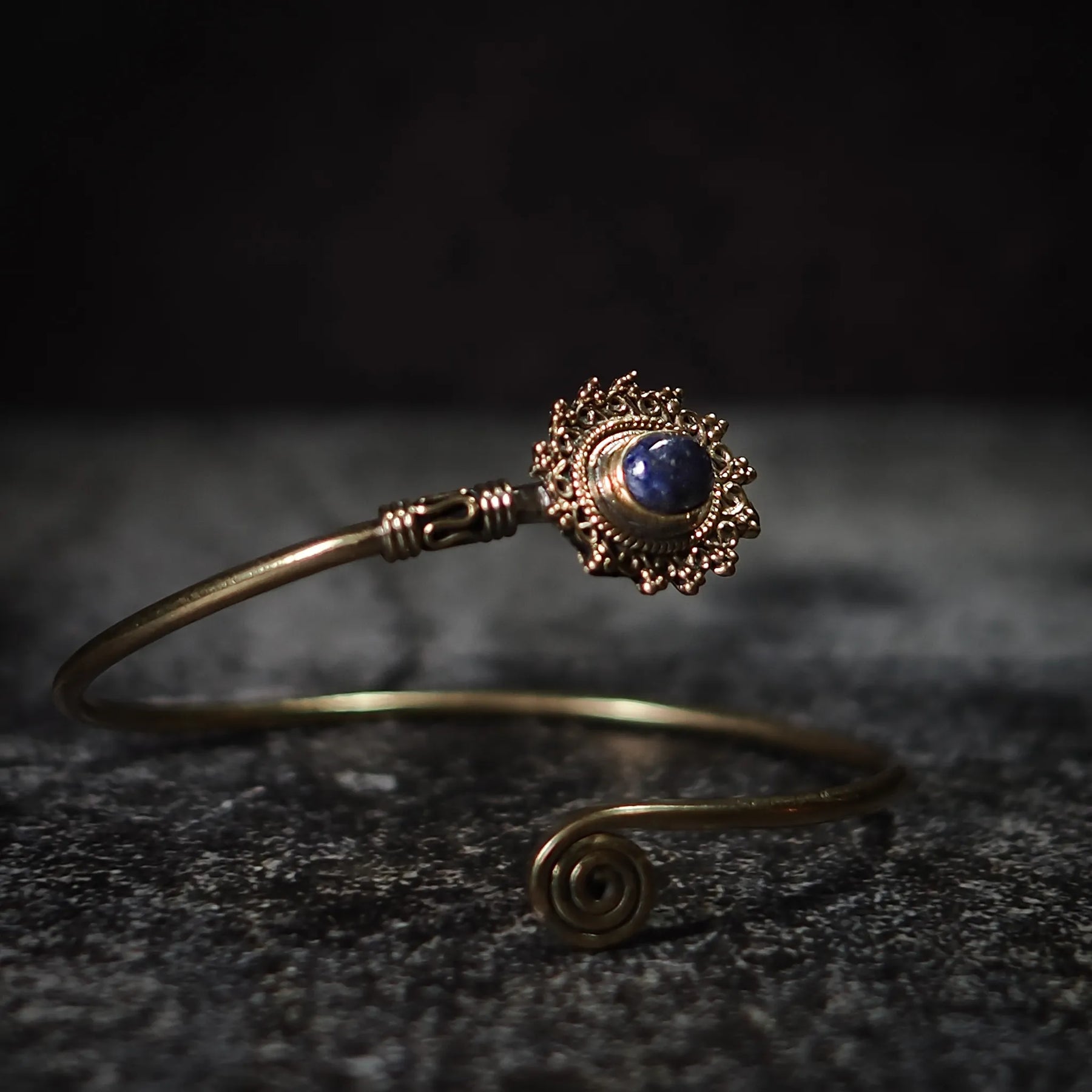 Vikingarmband i mörkblå halvädelsten med dekorativ mässingfiligre och spiralformad terminal på mörk bakgrund