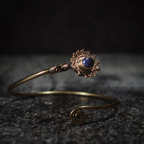Vikingarmband i mörkblå halvädelsten med dekorativ mässingfiligre och spiralformad terminal på mörk bakgrund