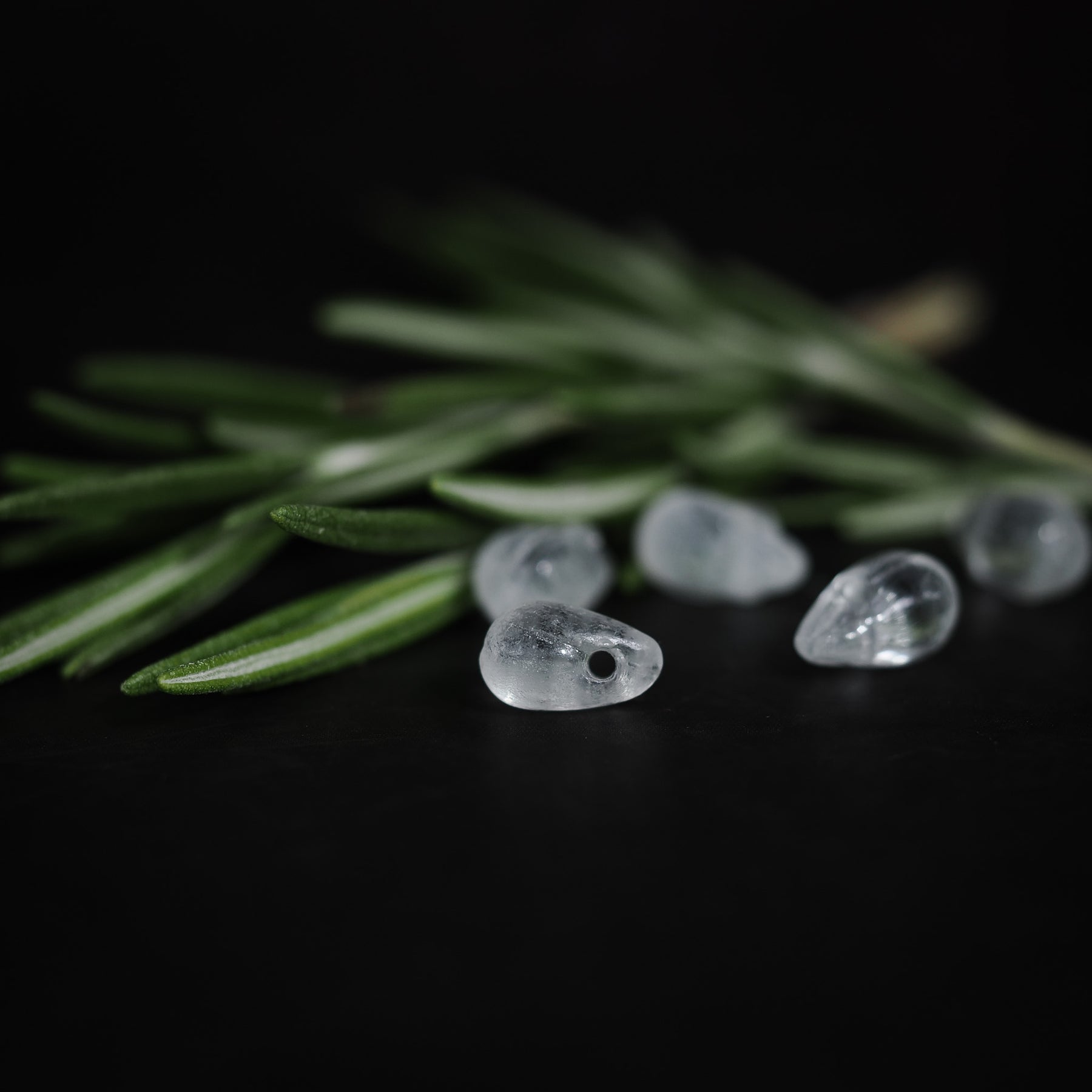 Droppformade glaspärlor arrangerade bland barrträdsgrenar, närbildsfotografi med fokus på klarhet och detaljer