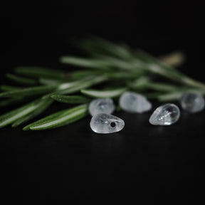 Droppformade glaspärlor arrangerade bland barrträdsgrenar, närbildsfotografi med fokus på klarhet och detaljer