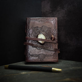 Liten läderbok Kristall stängd från sidan, visar präglad vikingamönster på mörkt skinn med vit Lapis Lazuli-sten och läderstöppe