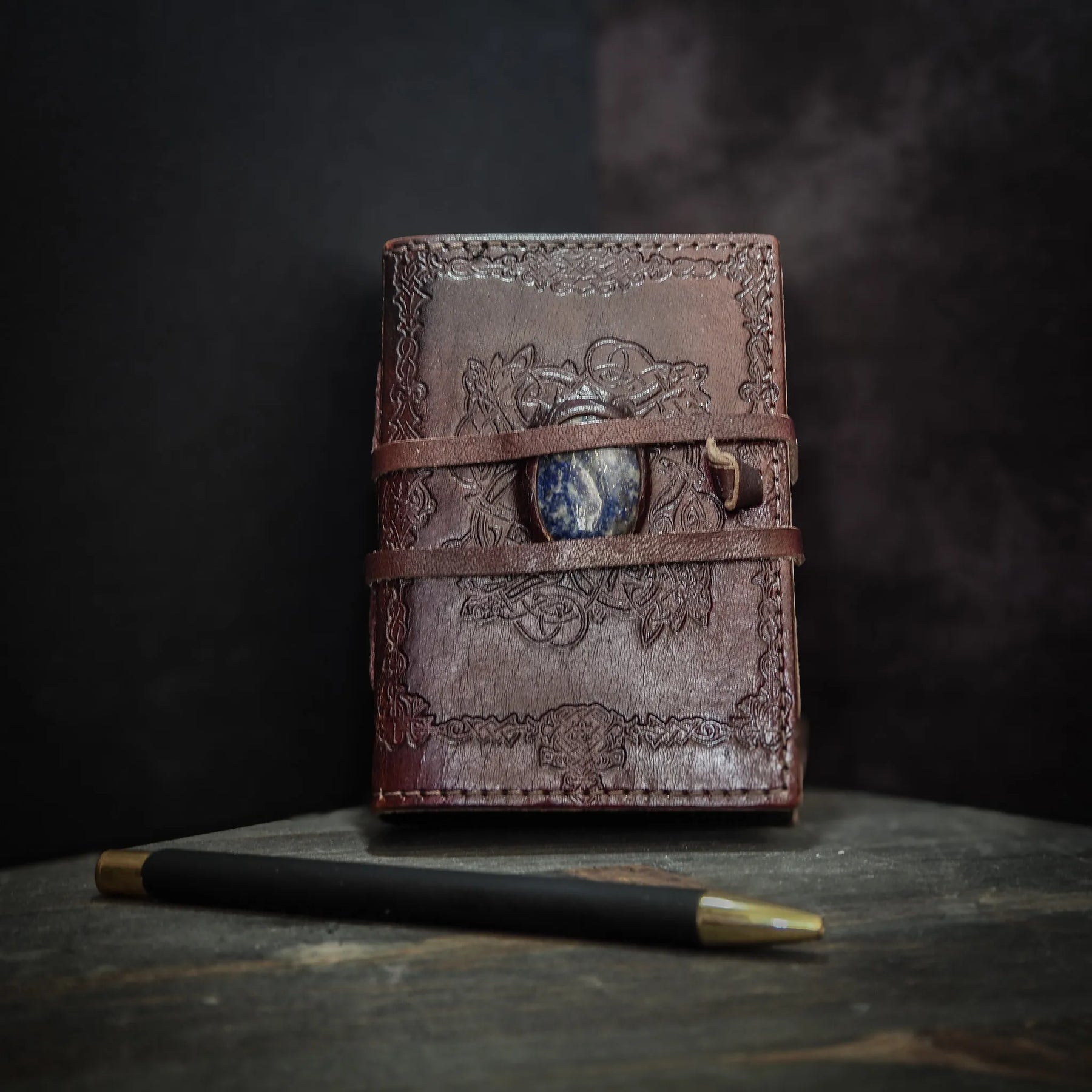 Liten läderbok Kristall stängd, visar stampad vikingamönster på brunt skinn med inlagd Lapis Lazuli och läderstöppe