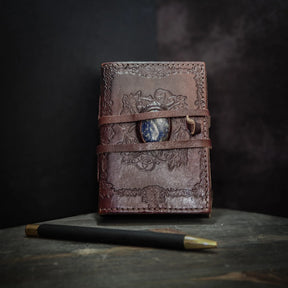 Liten läderbok Kristall stängd, visar stampad vikingamönster på brunt skinn med inlagd Lapis Lazuli och läderstöppe