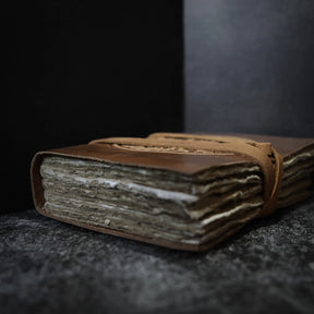 Stängd läderband anteckningsbok fotograferad från sidan, visar tjockleken på 100-arks bomullspappret och läderremmen