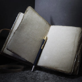 Öppen anteckningsbok med handgjort bomullspapper och läderband, en penna placerad på sidorna för att visa skrivkvaliteten
