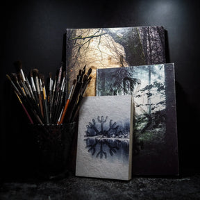 Målarbok A4 med Vegvisir-motiv och höstskogsbakgrund, omgiven av målarpensel i svart behållare